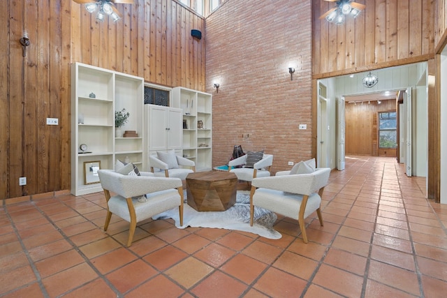 living area featuring plenty of natural light, wooden walls, a high ceiling, and a ceiling fan