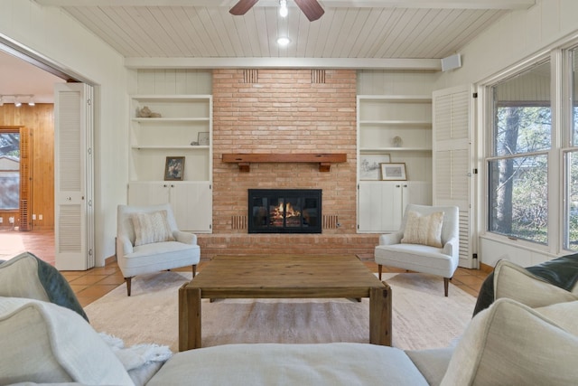 living room featuring a brick fireplace, built in shelves, beamed ceiling, and tile patterned floors