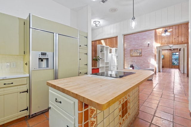 kitchen with butcher block countertops, paneled refrigerator, backsplash, and black electric stovetop