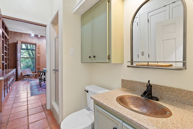 full bath with toilet, wooden walls, vanity, a stall shower, and rail lighting