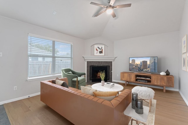 living room with a tiled fireplace, wood finished floors, baseboards, ceiling fan, and vaulted ceiling