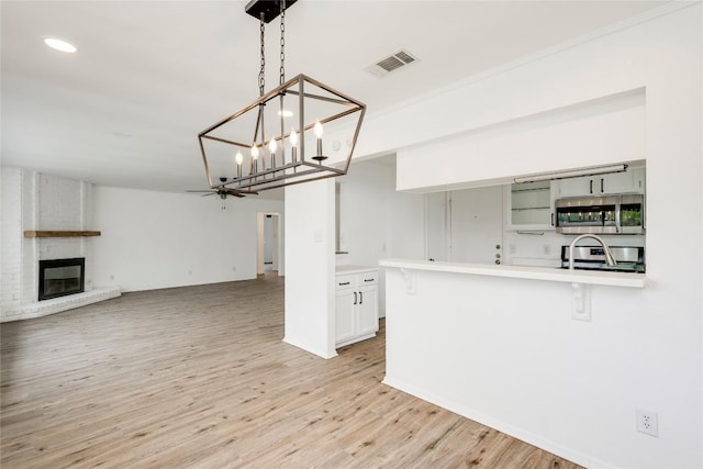 6705 Lancret Hill Dr, Austin, TX 78745 - kitchen featuring stainless steel microwave, light countertops, light wood-style flooring, a fireplace, and a kitchen breakfast bar