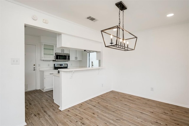6705 Lancret Hill Dr, Austin, TX 78745 - kitchen featuring appliances with stainless steel finishes, a breakfast bar, light wood-style flooring, light countertops, and a chandelier