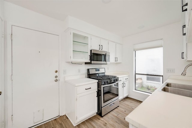 kitchen with light countertops, white cabinets, stainless steel appliances, a sink, and light wood-type flooring