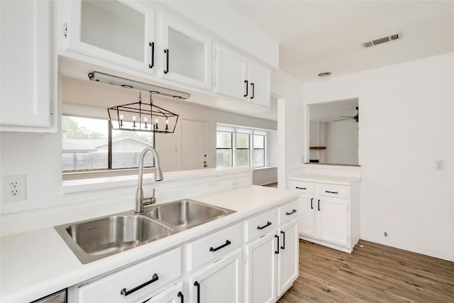 kitchen with white cabinetry, light countertops, a sink, light wood finished floors, and visible vents