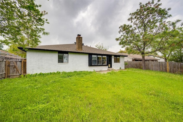 back of property featuring a chimney, fence, brick siding, and a yard