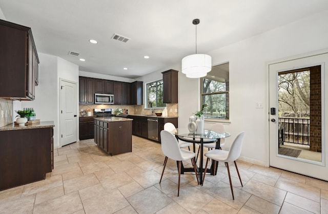 kitchen featuring visible vents, backsplash, appliances with stainless steel finishes, a kitchen island, and dark brown cabinets