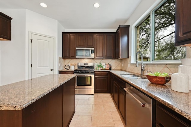 kitchen with light stone counters, dark brown cabinetry, a sink, appliances with stainless steel finishes, and backsplash