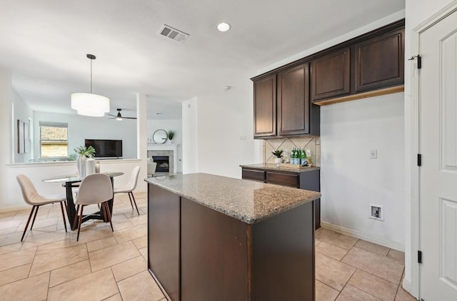 kitchen with stone counters, a center island, visible vents, backsplash, and dark brown cabinets