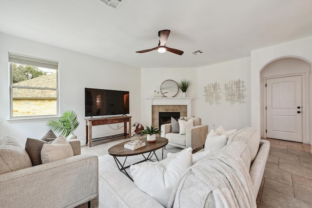 living room with ceiling fan, visible vents, arched walkways, and a tiled fireplace