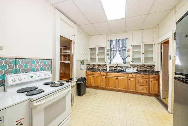 kitchen with electric range, brown cabinetry, a drop ceiling, glass insert cabinets, and a sink