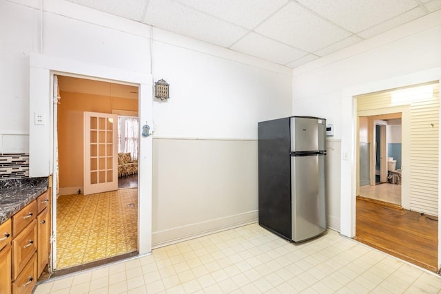 kitchen with brown cabinets, light floors, a paneled ceiling, freestanding refrigerator, and baseboards