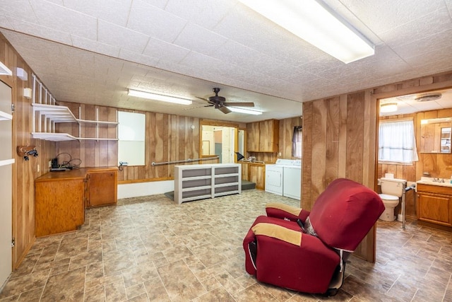 living area featuring stone finish flooring, wooden walls, a ceiling fan, and independent washer and dryer