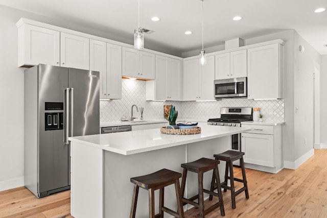 kitchen with a breakfast bar area, stainless steel appliances, white cabinets, light countertops, and light wood finished floors