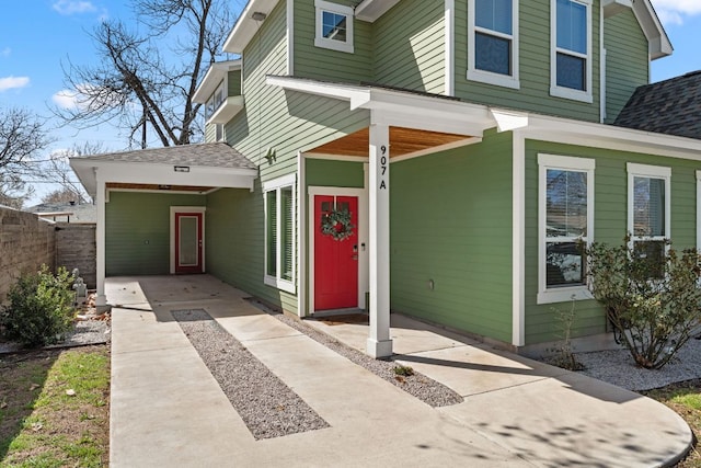 view of exterior entry featuring a shingled roof and fence