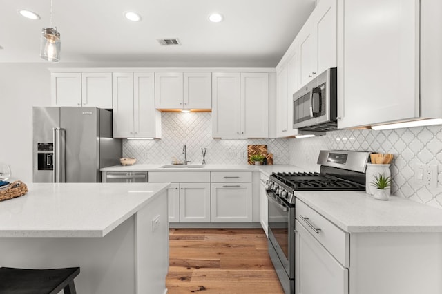 kitchen with stainless steel appliances, visible vents, white cabinets, a sink, and a kitchen bar