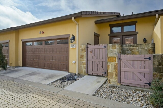 view of property exterior featuring a gate, driveway, an attached garage, and stucco siding