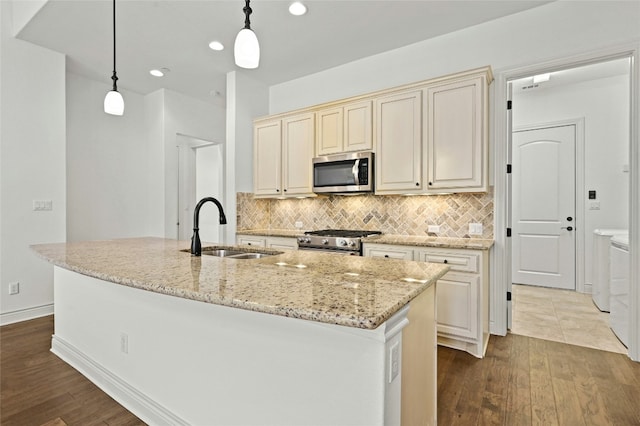 kitchen featuring tasteful backsplash, appliances with stainless steel finishes, light stone countertops, cream cabinetry, and a sink