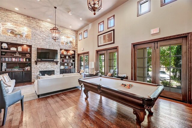 rec room with a stone fireplace, a towering ceiling, hardwood / wood-style flooring, and a healthy amount of sunlight