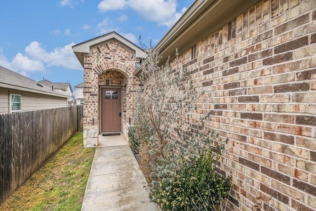 view of exterior entry with brick siding and fence