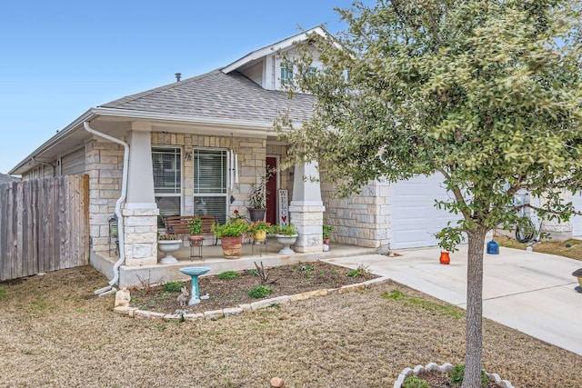 view of front of house featuring driveway, stone siding, fence, and a porch