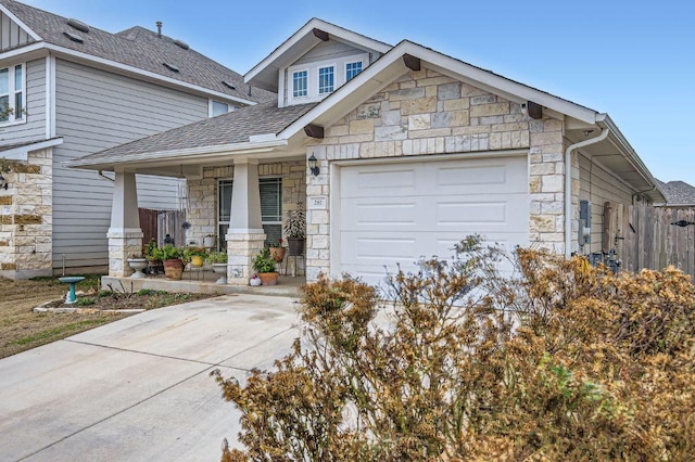 view of front of home featuring driveway, stone siding, roof with shingles, an attached garage, and fence