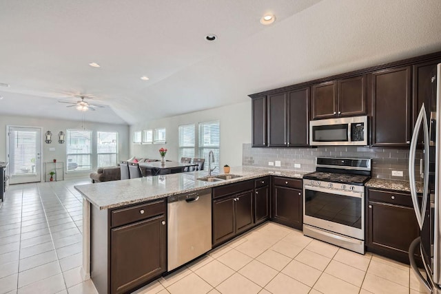 kitchen with light tile patterned floors, appliances with stainless steel finishes, a peninsula, dark brown cabinets, and a sink