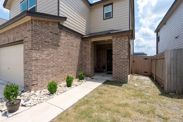 property entrance with a garage, fence, and brick siding