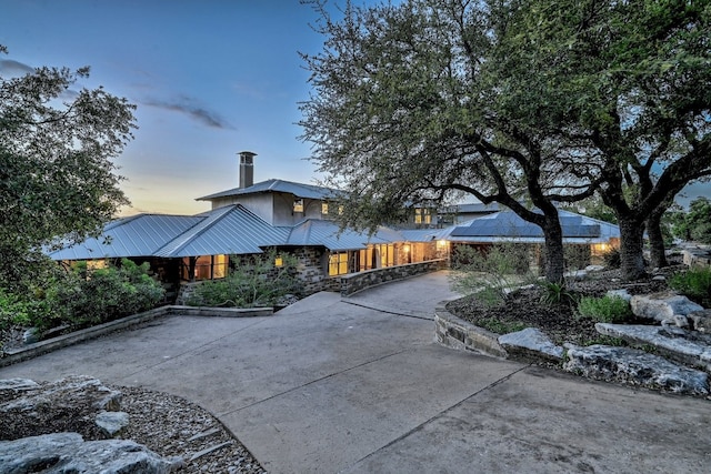 exterior space featuring a chimney, concrete driveway, a standing seam roof, metal roof, and stone siding