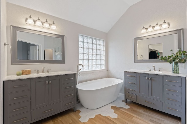 full bathroom with vaulted ceiling, a freestanding bath, two vanities, and a sink