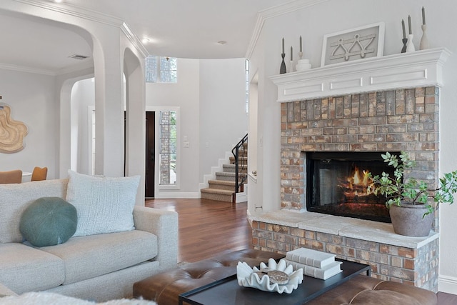 living area with ornamental molding, stairs, a fireplace, and wood finished floors