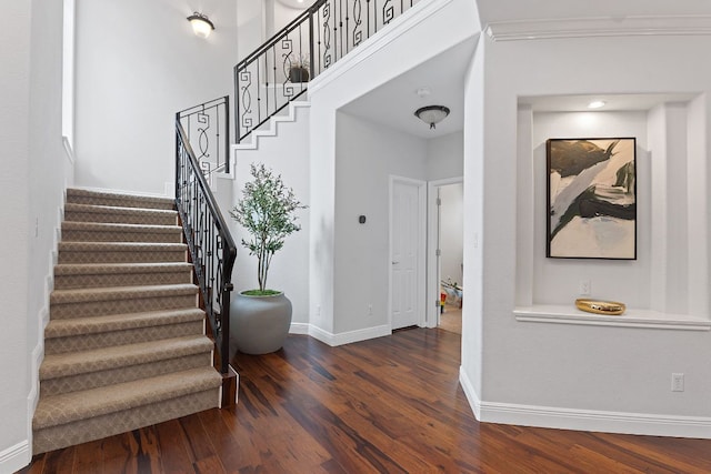 staircase featuring ornamental molding, a high ceiling, wood finished floors, and baseboards