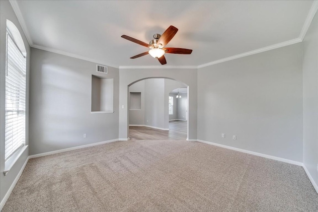 unfurnished room featuring arched walkways, visible vents, a ceiling fan, carpet, and crown molding