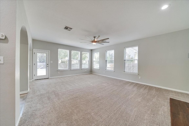 unfurnished living room featuring light carpet, baseboards, visible vents, arched walkways, and ceiling fan