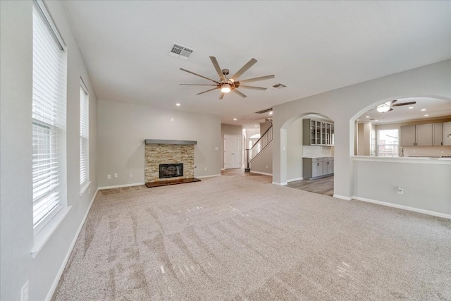 unfurnished living room with visible vents, arched walkways, a ceiling fan, a glass covered fireplace, and stairway