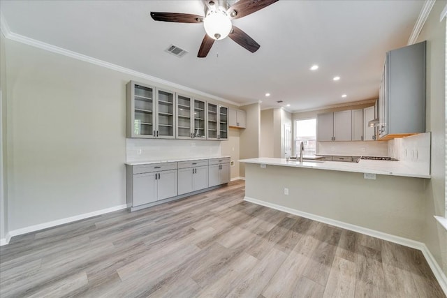 kitchen with crown molding, light wood-style flooring, gray cabinetry, a peninsula, and baseboards