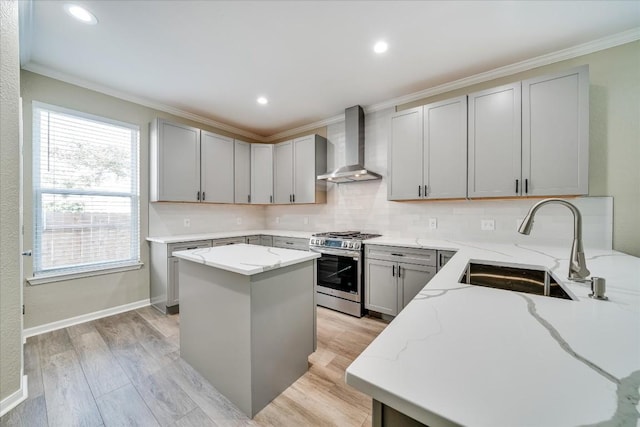 kitchen with gray cabinetry, a sink, wall chimney range hood, stainless steel range with gas cooktop, and light stone countertops