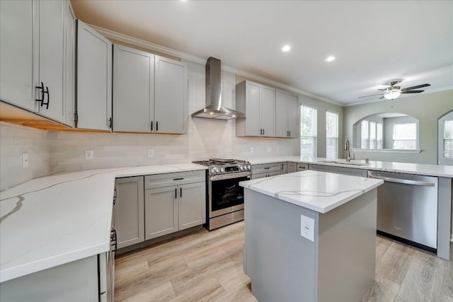 kitchen with gray cabinetry, appliances with stainless steel finishes, a sink, a peninsula, and wall chimney exhaust hood