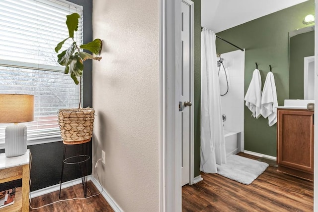 bathroom with a textured wall, shower / bath combo, wood finished floors, and baseboards