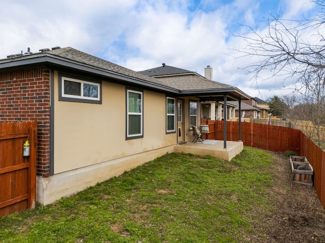 back of house featuring a lawn, a patio, roof with shingles, fence, and brick siding