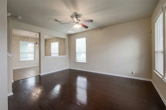 unfurnished room with a wealth of natural light, visible vents, ceiling fan with notable chandelier, and wood finished floors