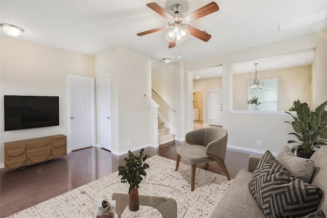 living area with ceiling fan with notable chandelier, stairway, wood finished floors, and baseboards