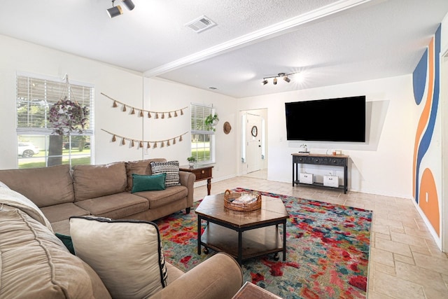 living room with stone tile flooring, visible vents, a textured ceiling, and baseboards