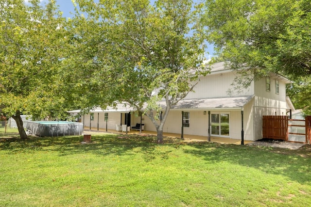 rear view of house with a yard, an outdoor pool, and fence