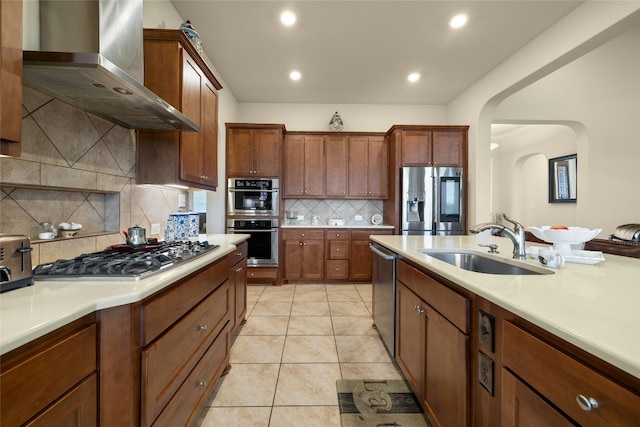 kitchen featuring wall chimney range hood, stainless steel appliances, a sink, and light countertops