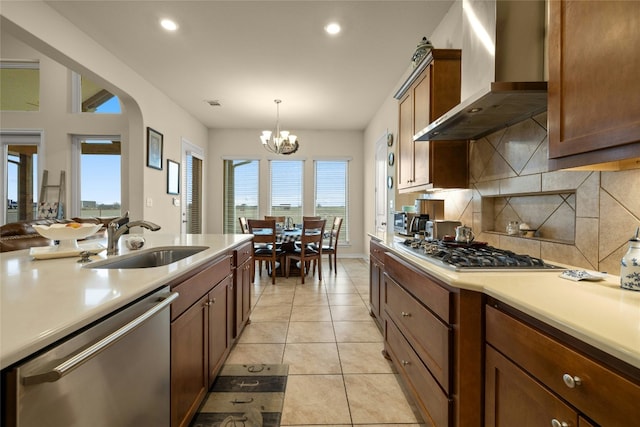 kitchen featuring appliances with stainless steel finishes, light countertops, a sink, and wall chimney exhaust hood