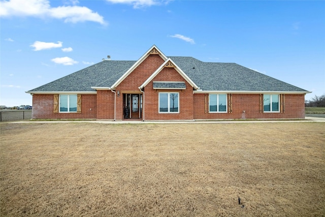 back of house featuring roof with shingles, a lawn, and brick siding