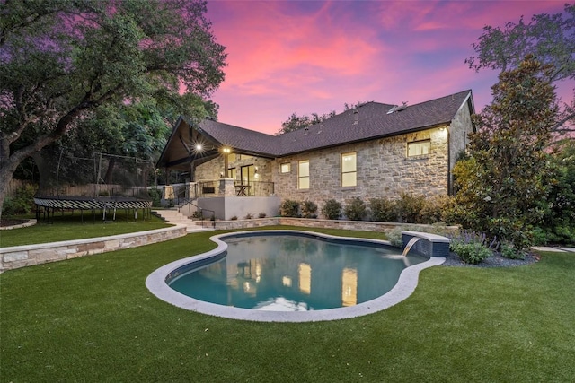 rear view of property with stone siding, a trampoline, an outdoor pool, and a yard