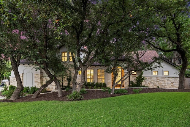 view of front of house featuring a front yard, stone siding, and stucco siding