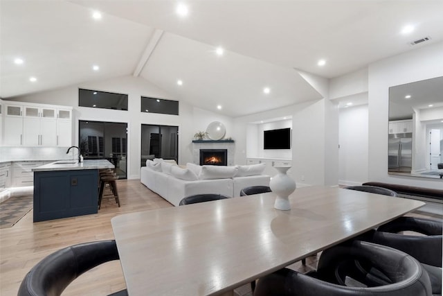 dining space featuring recessed lighting, visible vents, light wood-style floors, a lit fireplace, and beam ceiling